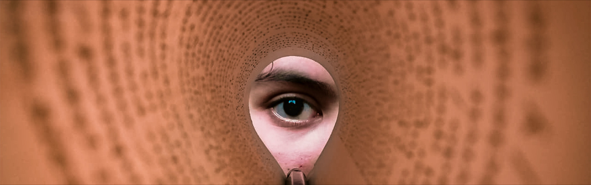 A person's eye looking through a rolled book page, creating a unique viewpoint.